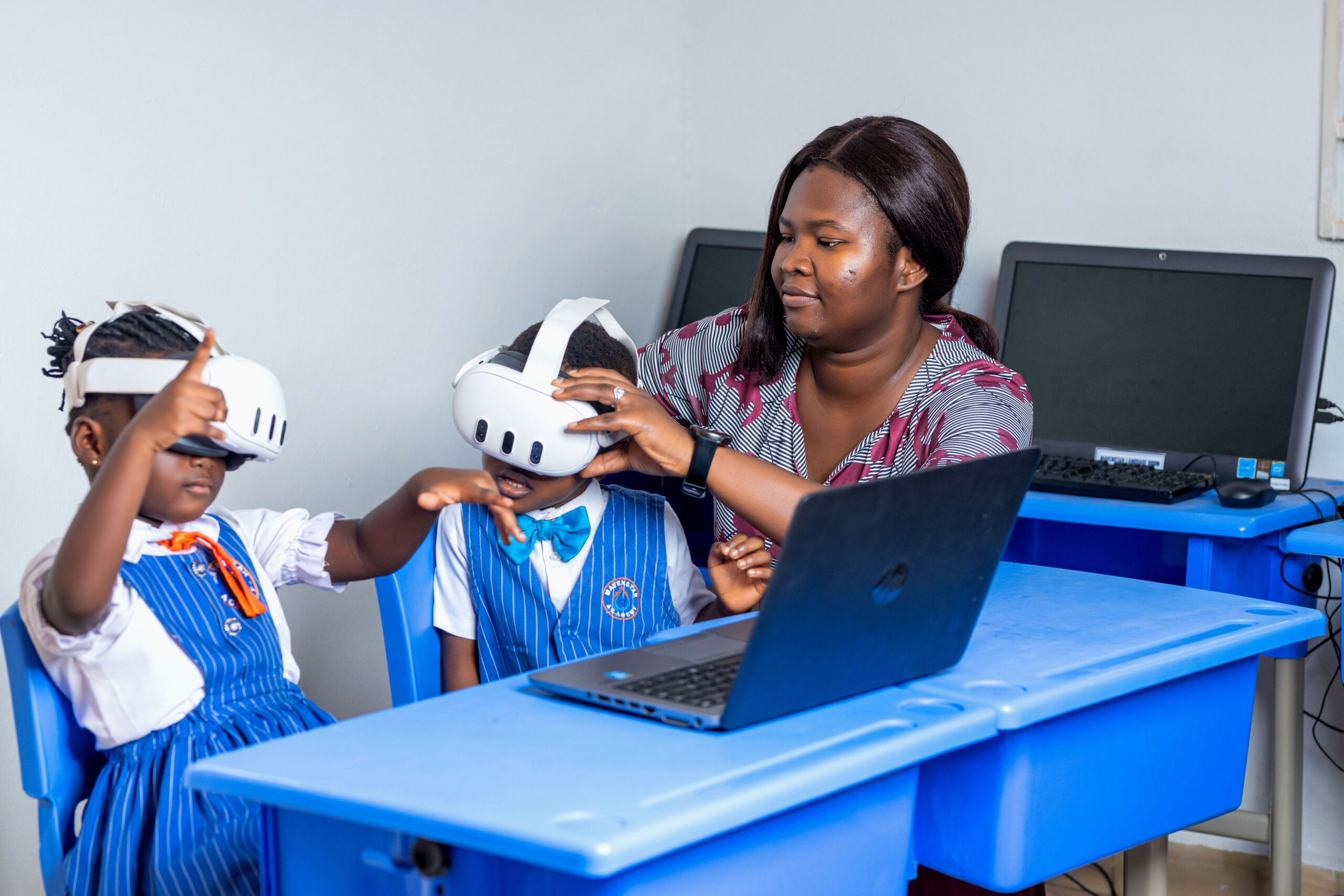 A teacher fitting VR headsets on two schoolchildren in a Ghanaian computer classroom